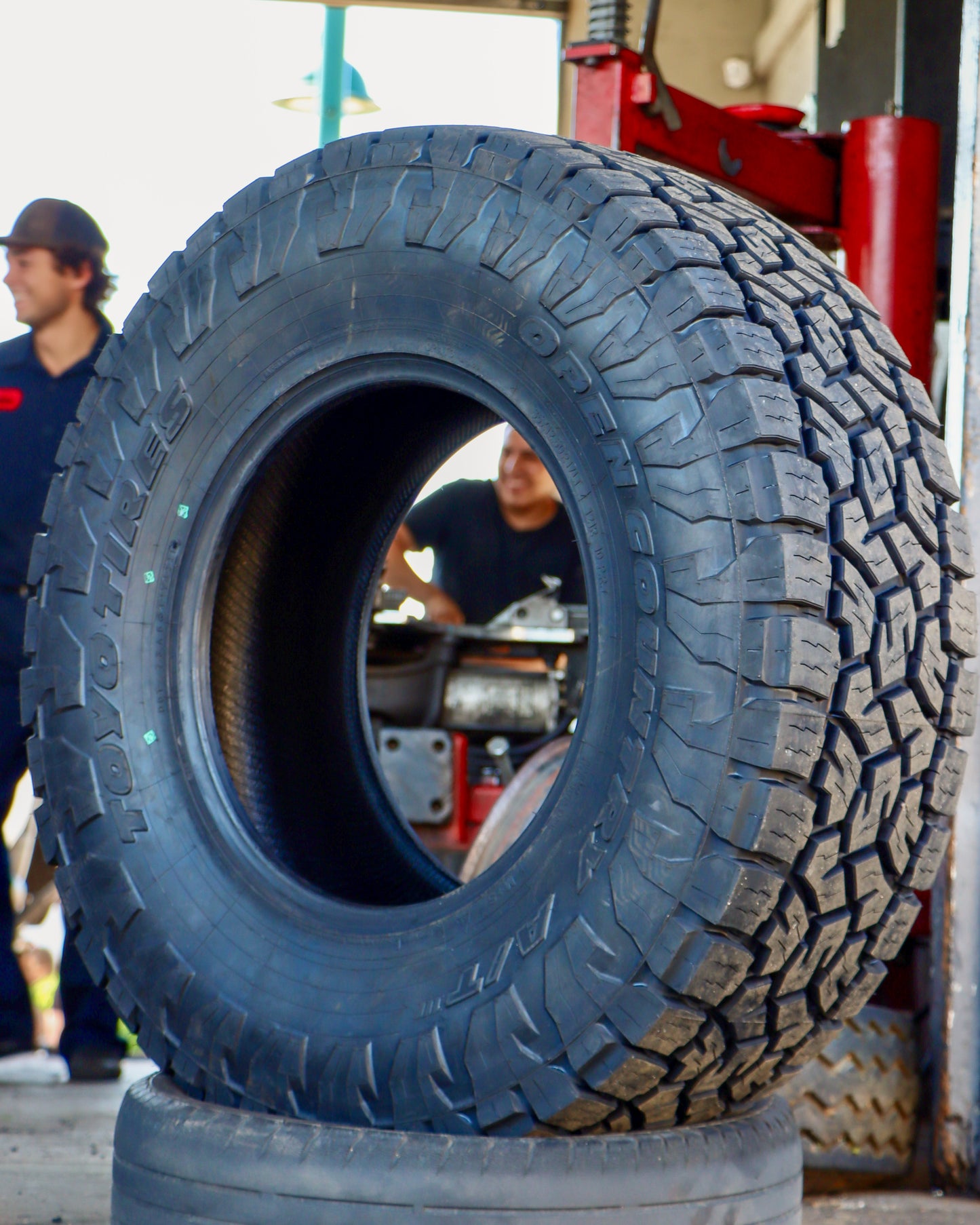 Toyo Open Country ATIII sitting in a smaller tire with tire machines in the background.