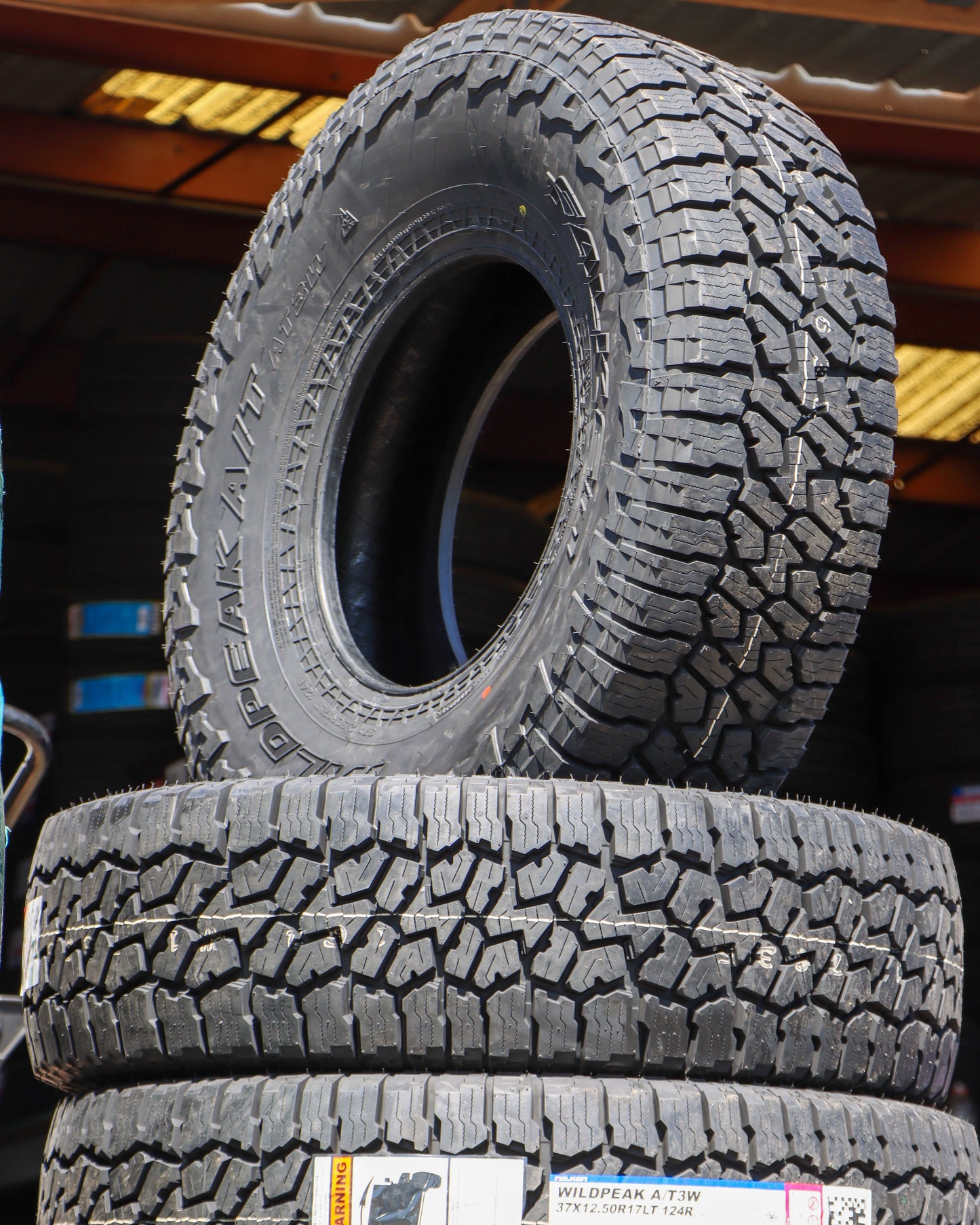 Stack of Falken Wildpeak AT3 tires with one standing up showing the tread and side-wall.