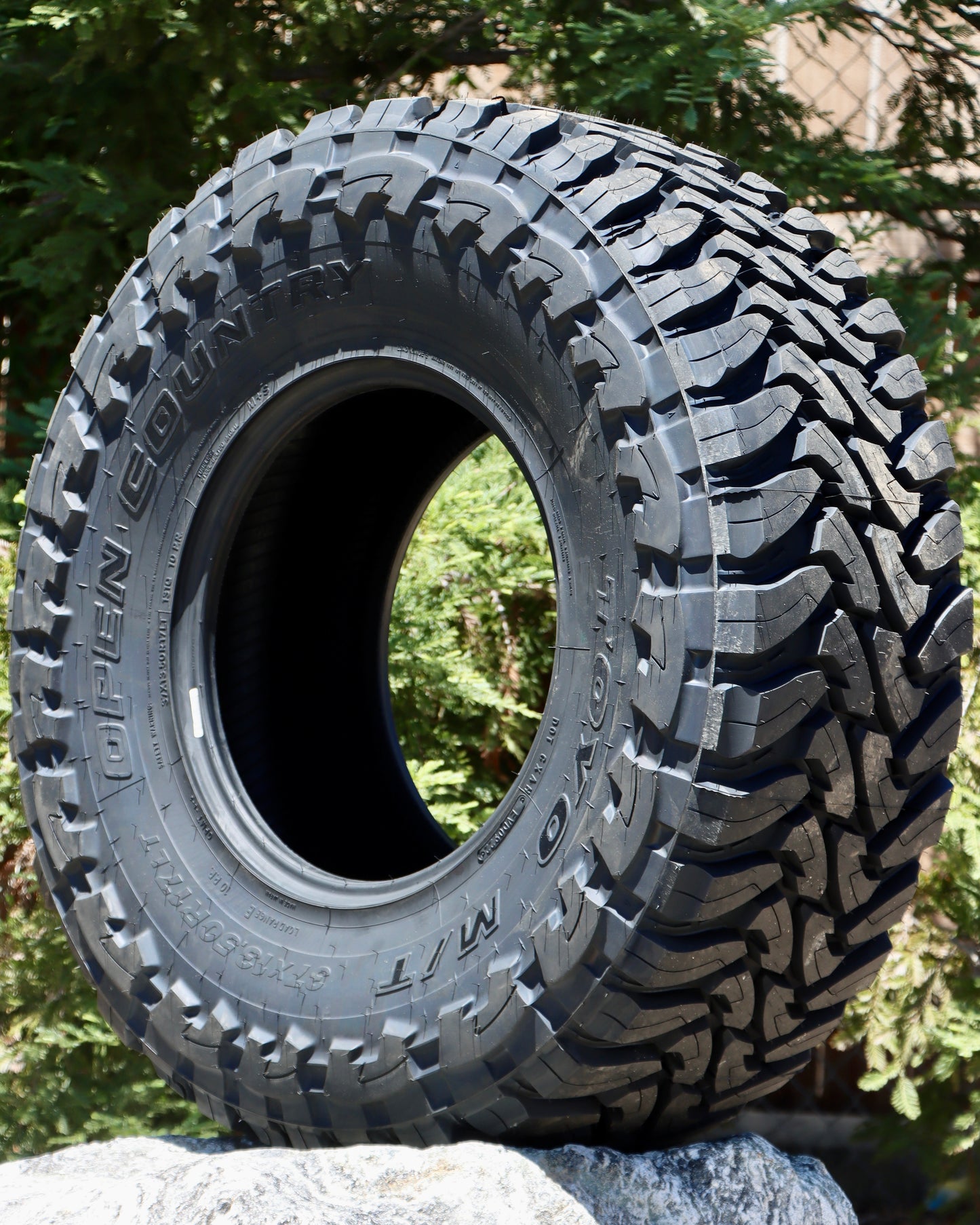 Toyo Open Country M/T tire sitting on a rock with pine trees in the background.