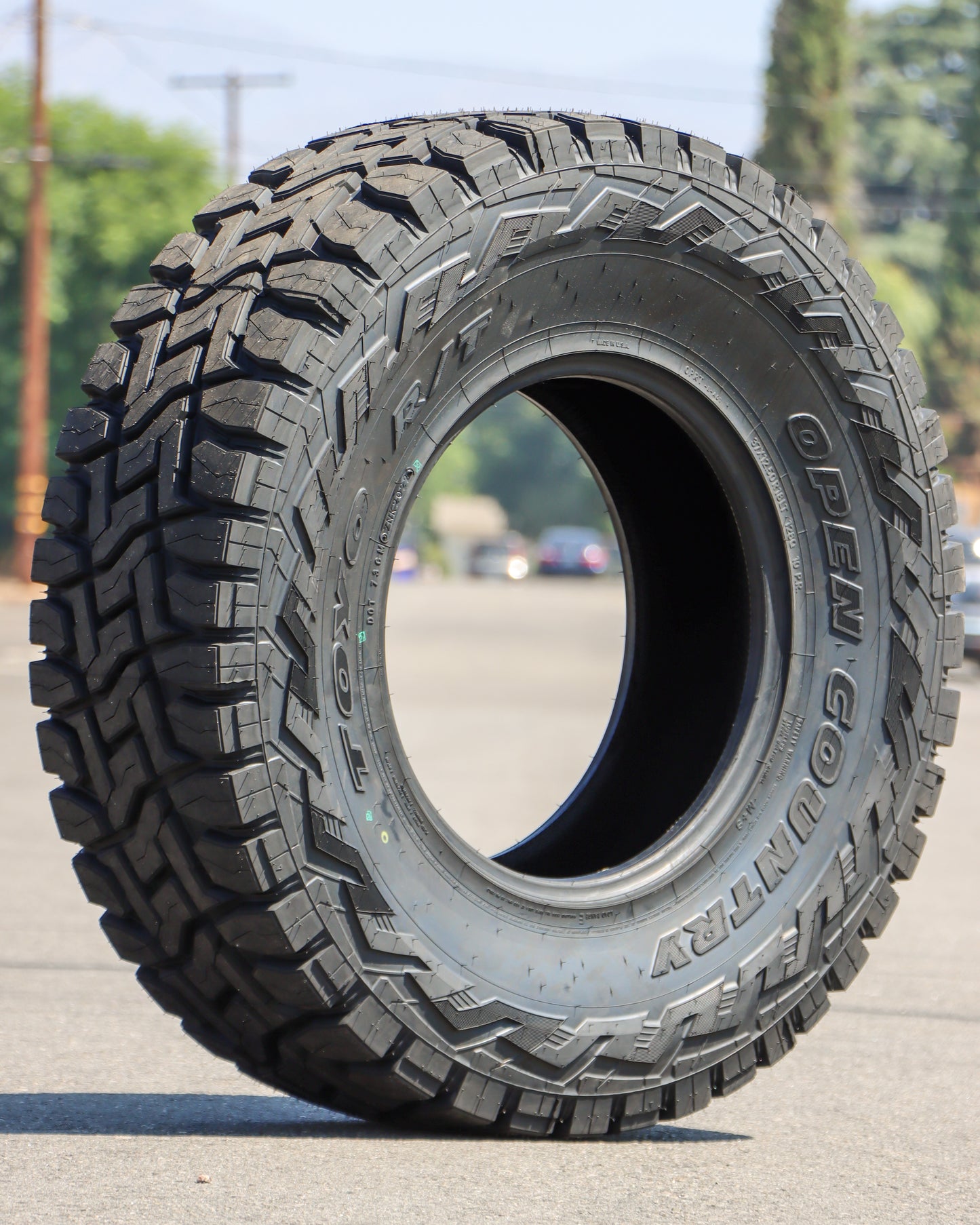 Toyo Open Country R/T tire sitting in the middle of the street with trees and powerlines in the background.