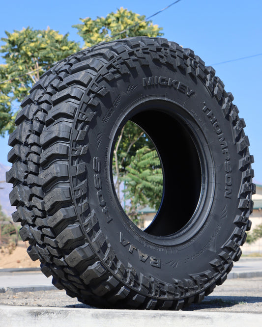Mickey Thompson baja boss tire sitting on the sidewalk with a tree and powerlines in the sbackground.