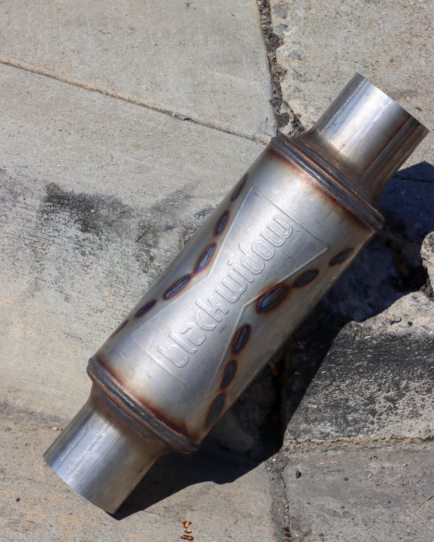 Black Widow Widowmaker 10-inch Series muffler leaning against a curb.