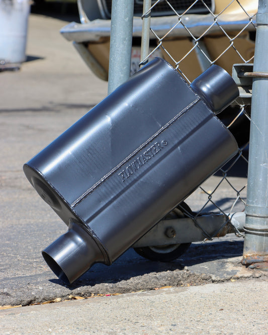 Flowmaster 40 Series Chambered Muffler Leaning against a chain link fence.