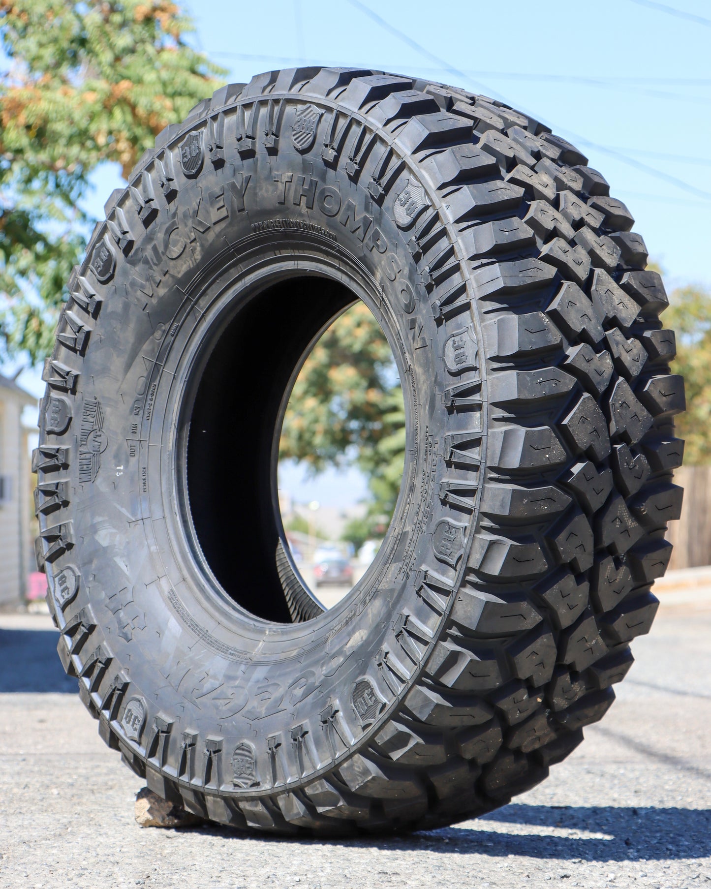 Mickey thompson Deagan 38 tire sitting in the middle of an alley with trees in the background.