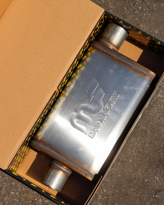 MagnaFLow Muffler in the box, lying flat on the ground with the box open.
