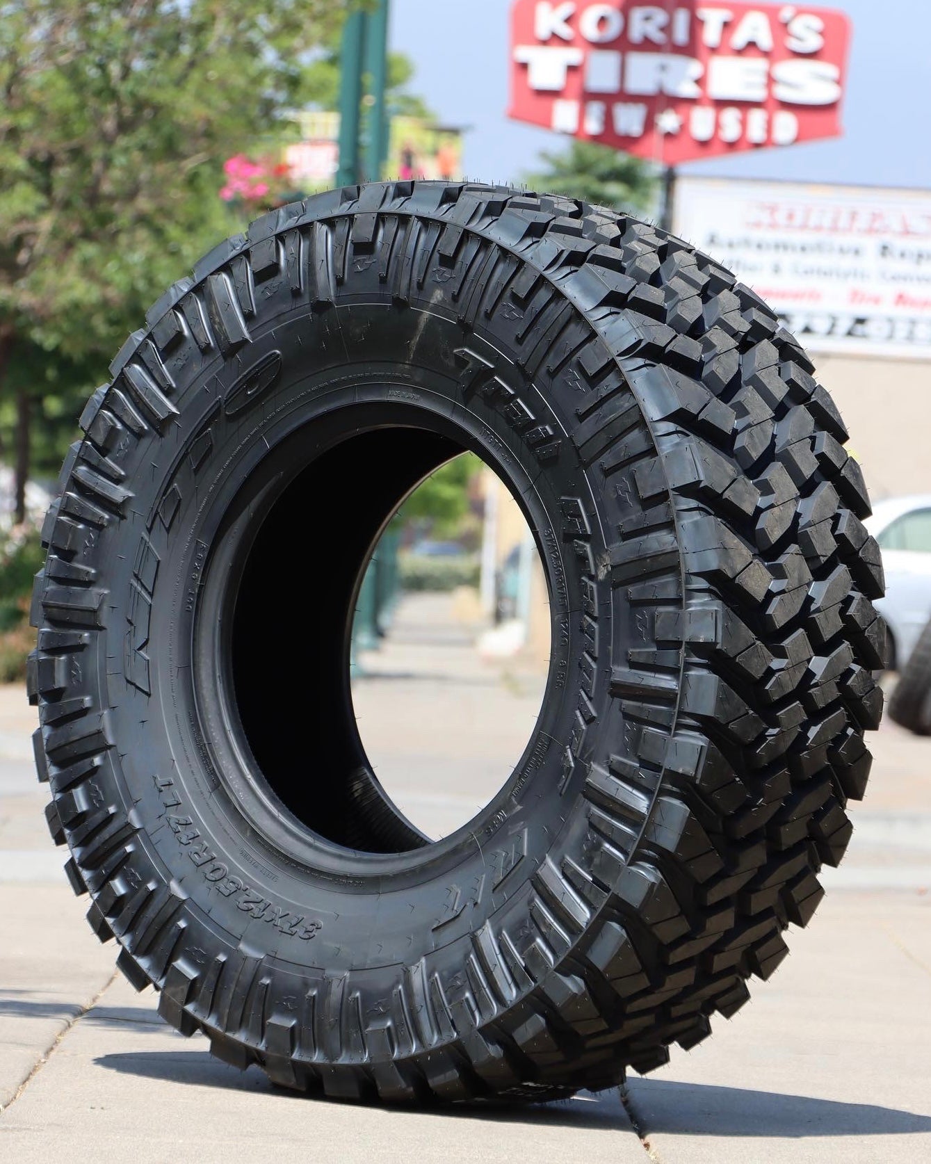 nitto trail grappler tire sitting in the middle of a sidewalk with the koritas tires sign in the background.