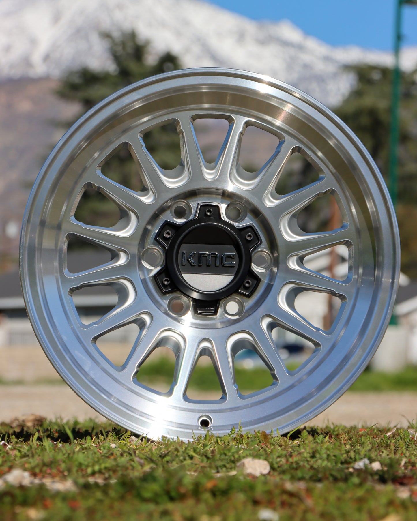 KMC Impact OlL Wheel in a silver Machined finish sitting in a field with mountains in the background.