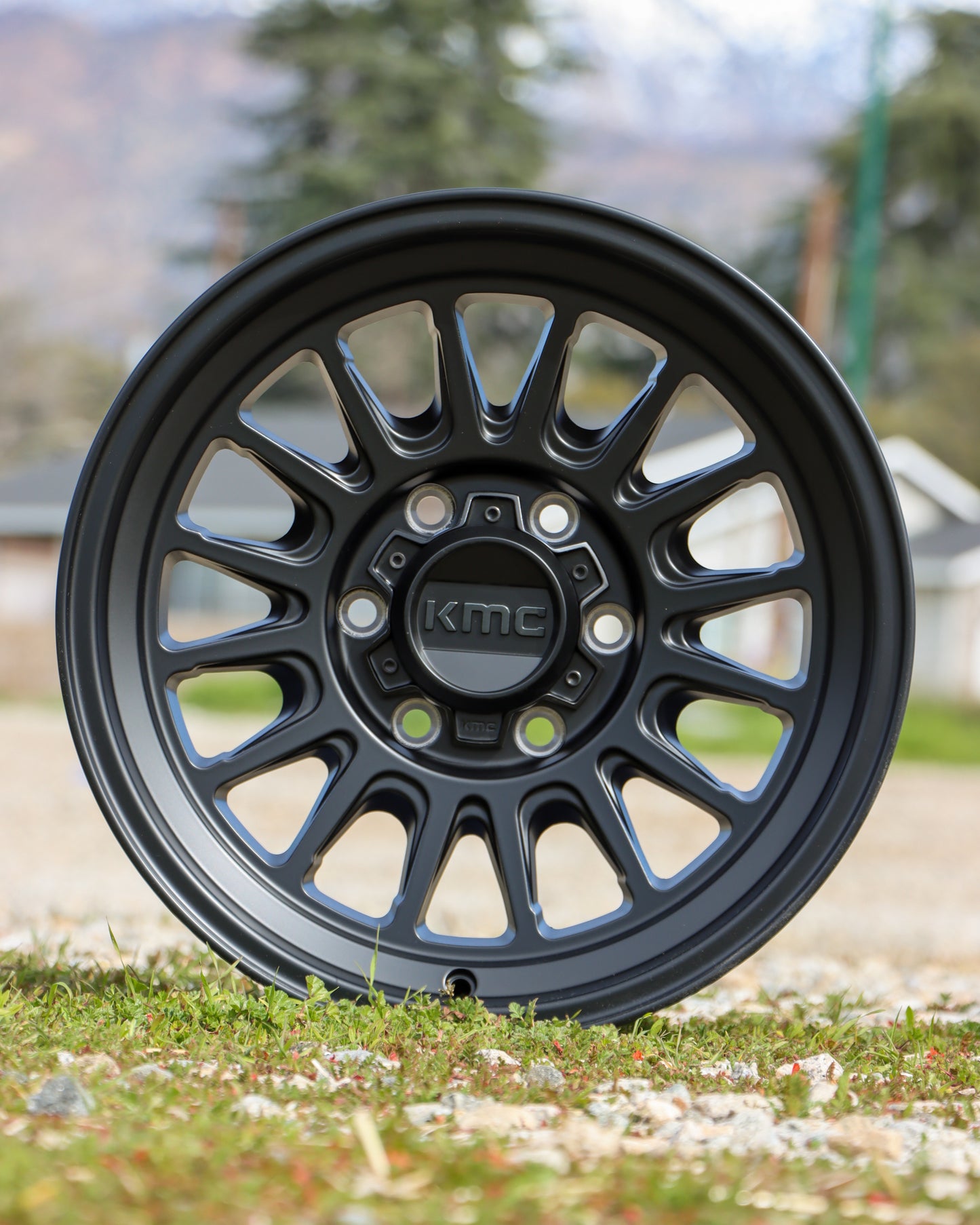 KMC Impact OL in a satin black finish, sitting in a field with trees in the background.