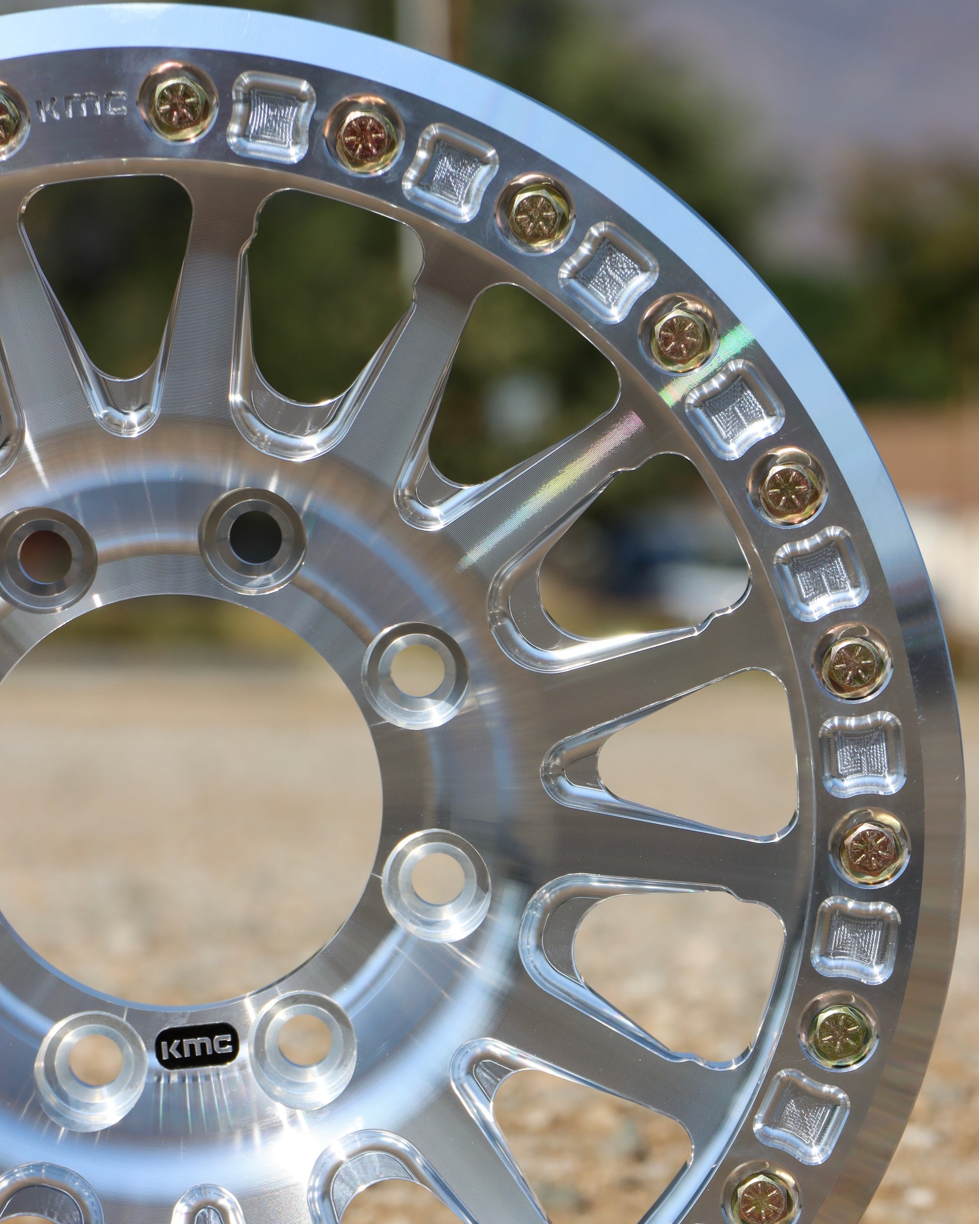 Close-up of the kmc impact forged bead lock wheel with blurred trees in the background.