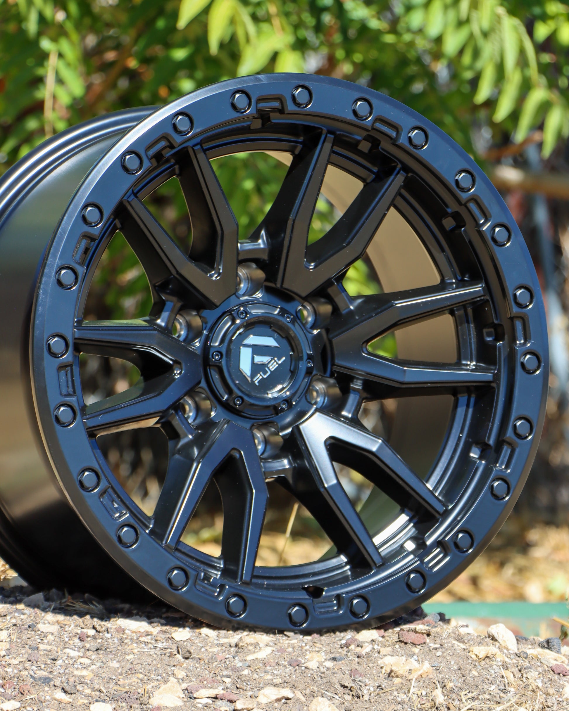 Fuel Rebel Wheel in matte black, at an angle on the ground with dirt and rocks under it.