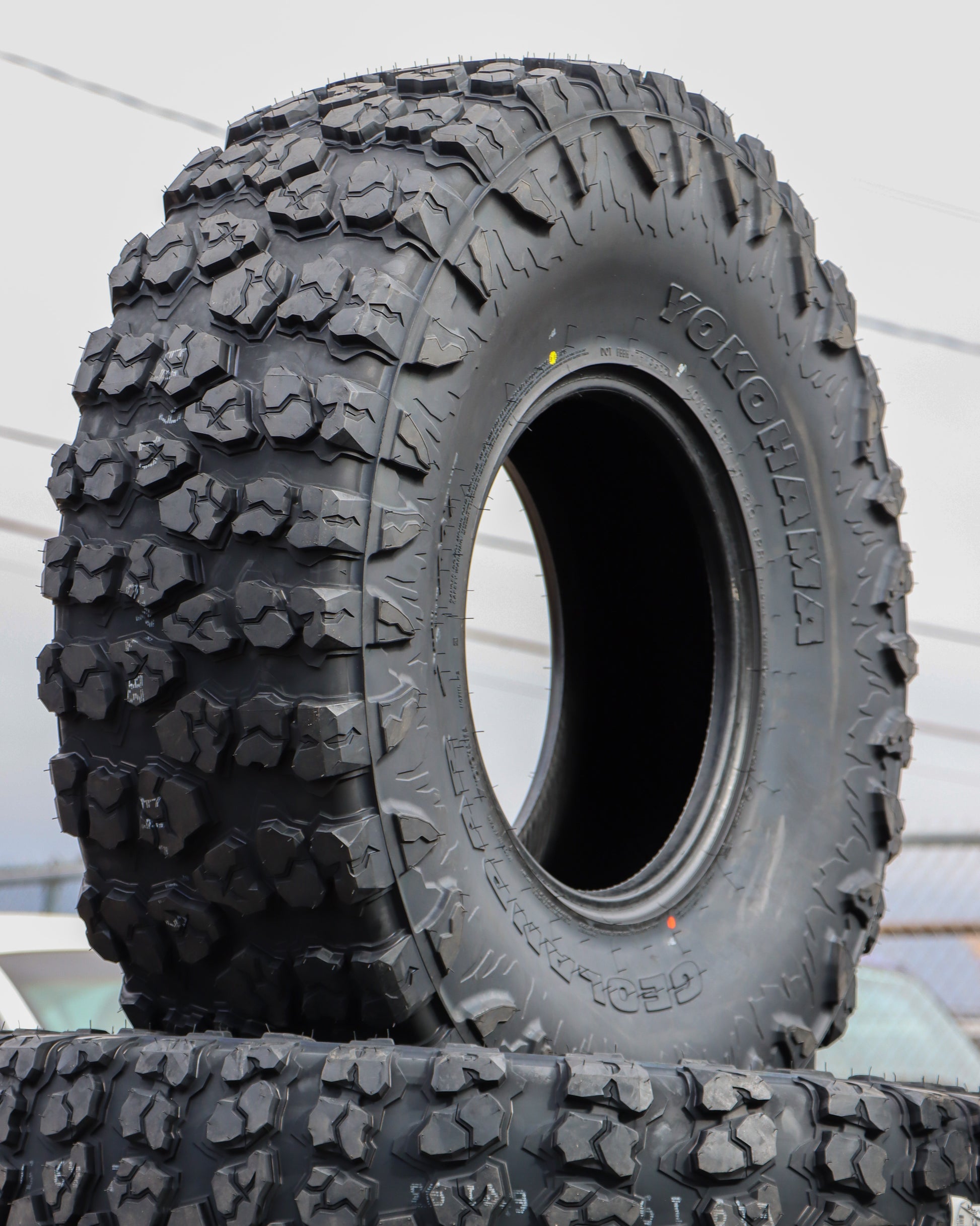 Yokohama Geolandar x-mt tire stacked up on other tires showing off the sidewall and tread of the tire.