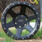 Dirty Life Compound Wheel Sitting in some dirt surrounded by grass, in a matte black finish.