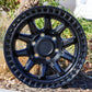 The Black Rhino Calico Wheel in a matte black finish sitting in a planter.