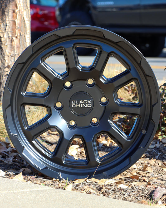 The Black Rhino Chase Wheel in a matte black finish sitting in a planter of woodchips.