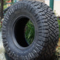 nitto ridge grappler tire sitting in a planter with a lot of bushes and trees in the background.