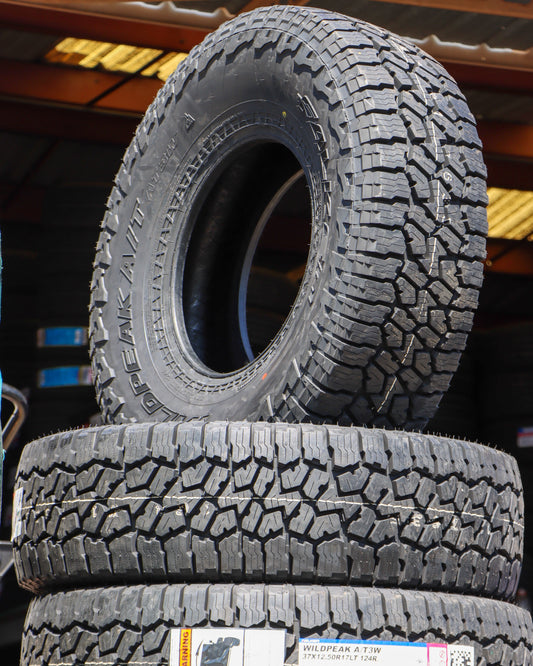 Stack of Falken Wildpeak AT3 tires with one standing up showing the tread and side-wall.