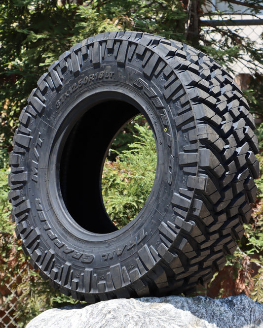 Nitto Trail Grappler tire set up on a rock with pine trees in the background.
