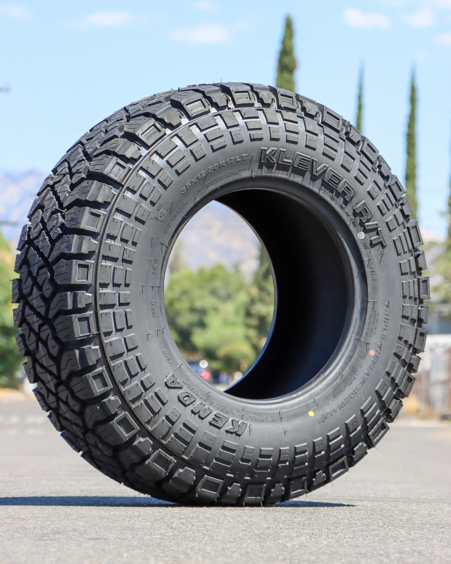 Kenda Klever R/T tire in the middle of the street with the sky and a couple trees in the Background.