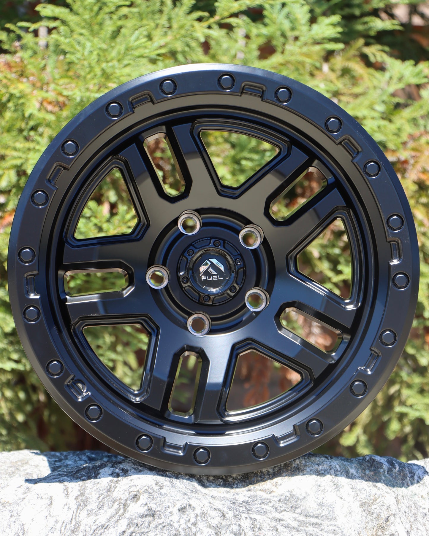 Fuel Ammo Wheel in a matte black finish sitting on a rock with trees in the background.