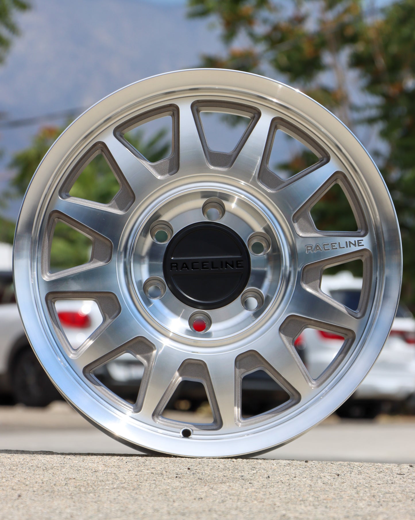 Raceline Areo wheel in a machined finish sitting on the ground with cars and trees in the background.