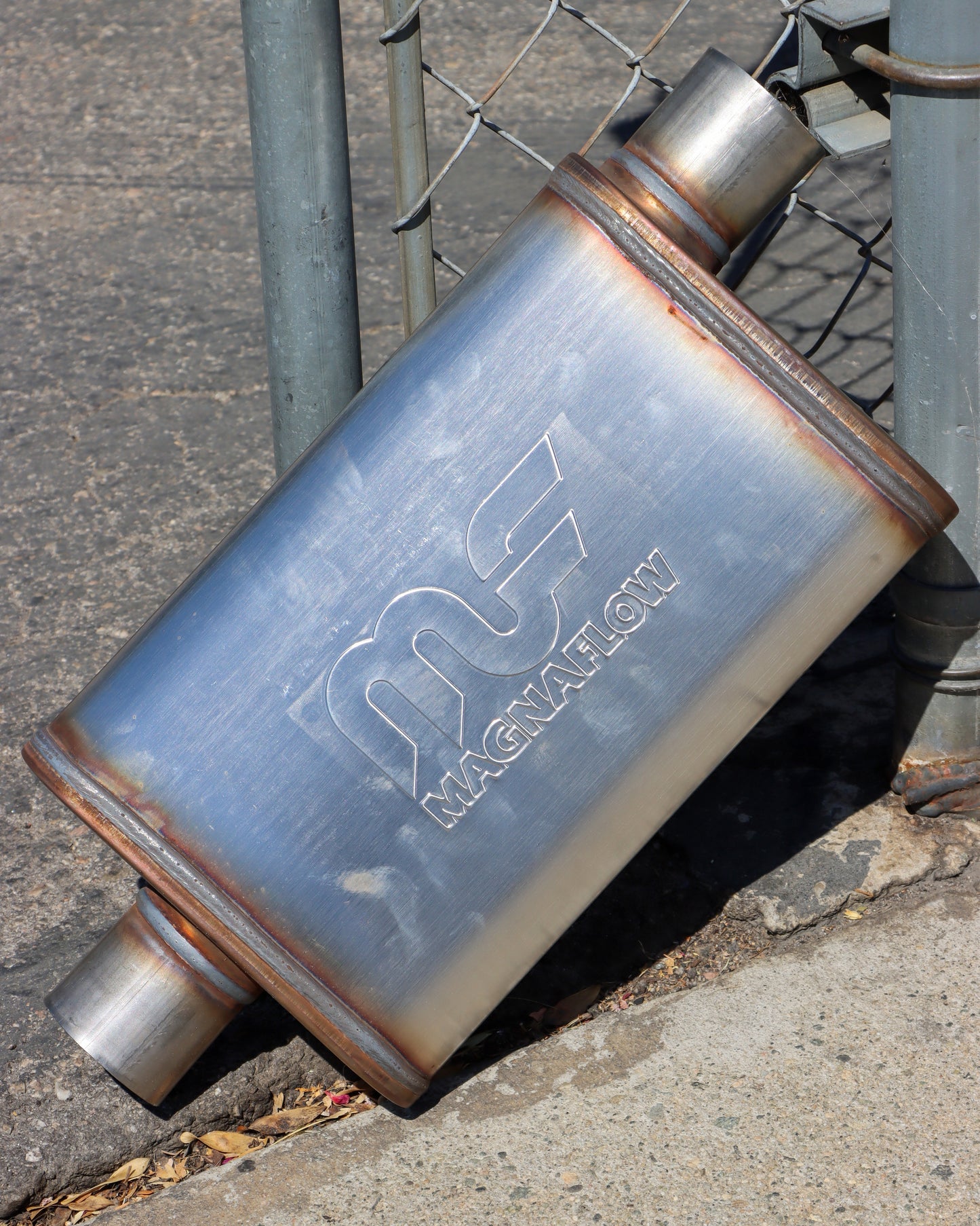 Magnaflow muffler leaning up against a chain link fence.